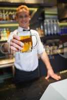 Smiling bartender offering pint of beer to camera