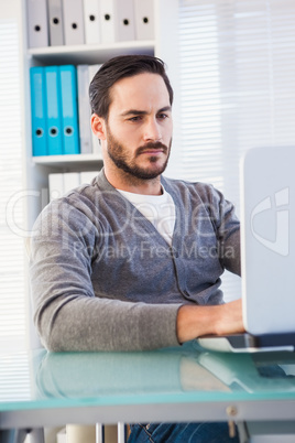 Serious casual businessman working on laptop at his desk