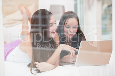 Pretty friends using laptop on bed