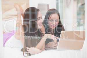 Pretty friends using laptop on bed