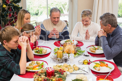 Extended family saying grace before christmas dinner