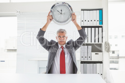 Mature businessman holding large clock