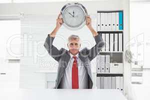Mature businessman holding large clock