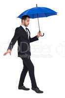 Concentrated businessman holding umbrella while stepping