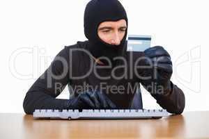 Burglar typing on keyboard and holding credit card