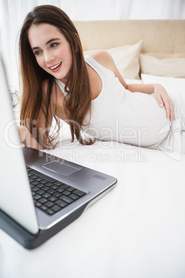 Pregnant brunette using laptop in bed