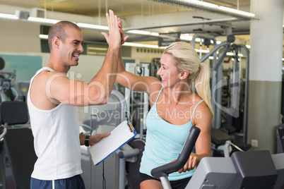 Trainer giving high five to his client on exercise bike at gym
