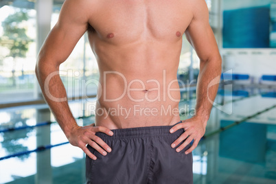 Mid section of a shirtless fit swimmer by pool at leisure center