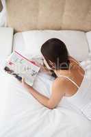 Pretty brunette reading magazine on bed