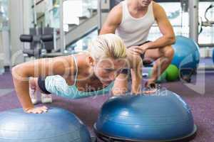 Male trainer assisting woman with push ups at gym