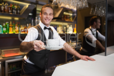 Smiling waiter offering cup of coffee smiling at camera