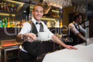 Smiling waiter offering cup of coffee smiling at camera