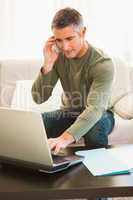 Man on the phone sitting on the couch and using laptop