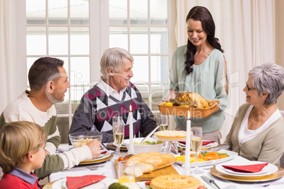 Woman holding turkey roast with family at dining table