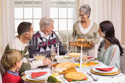 Grandmother holding turkey roast with family at dining table