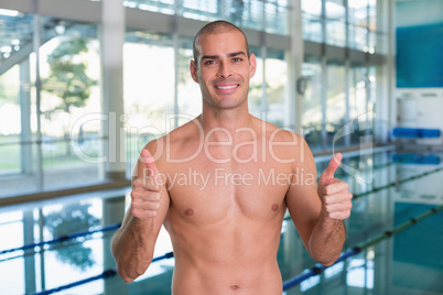 Fit swimmer gesturing thumbs up by pool at leisure center