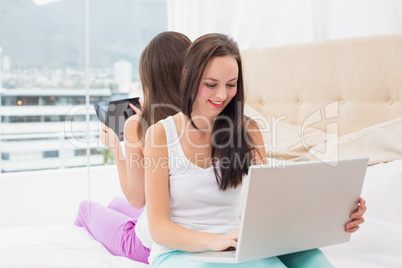 Pretty friends using their technology on bed