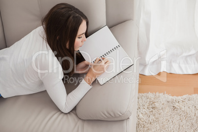 Pretty brunette writing in notepad on the sofa