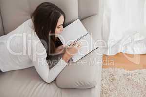 Pretty brunette writing in notepad on the sofa
