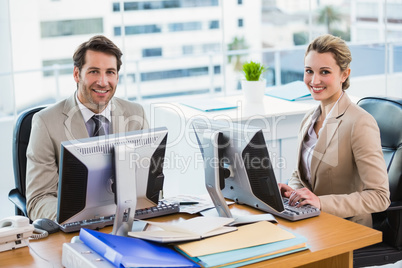 Business people using computer while looking at camera