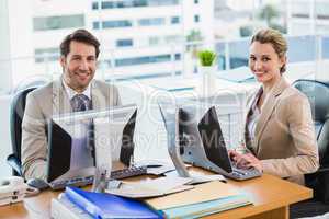 Business people using computer while looking at camera