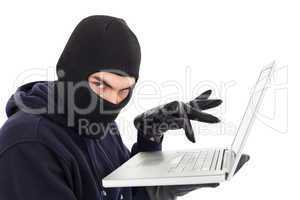 Hacker in balaclava standing and typing on laptop