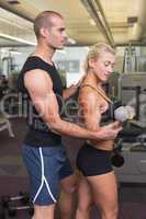 Male trainer assisting woman with dumbbell in gym