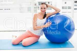 Fit brunette sitting beside exercise ball