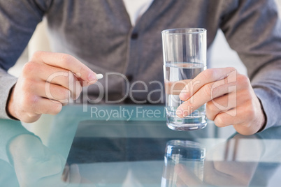 Close up of casual man holding a pill and glass of water