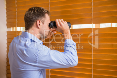 Man looking with binoculars through the blinds