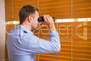 Man looking with binoculars through the blinds
