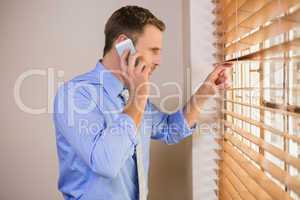 Businessman peeking through blinds while on call
