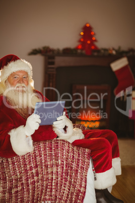 Smiling santa using tablet on the couch