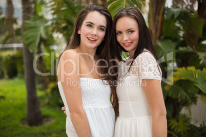 Pretty friends smiling at camera in white dresses