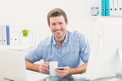 Smiling businessman holding mug and phone