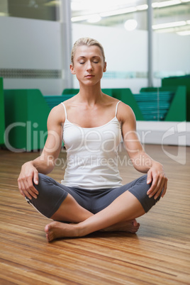 Sporty woman sitting with eyes closed in fitness studio