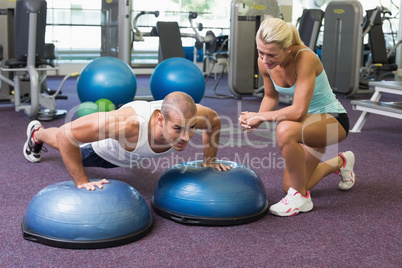 Trainer assisting man with push ups at gym