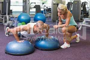 Trainer assisting man with push ups at gym