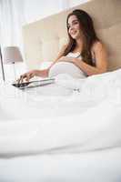 Pregnant brunette using laptop in bed