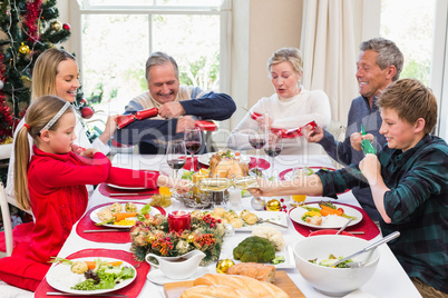 Family pulling christmas crackers at the dinner table