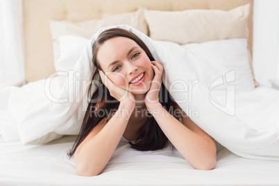 Pretty brunette smiling at camera in bed