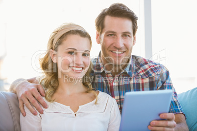 Couple using tablet pc on the couch while looking at camera