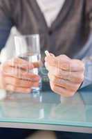 Mid section of a man holding glass of water and pill