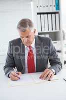 Mature businessman writing on document