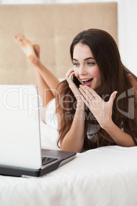 Pretty brunette on the phone in bed using laptop