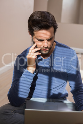 Depressed man sitting on floor using laptop