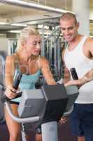 Trainer assisting woman with exercise bike at gym