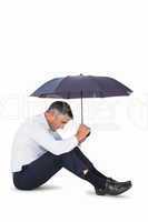 Businessman sitting and sheltering with umbrella