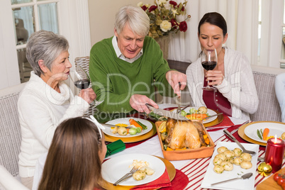 Grandfather carving chicken while women drinking red wine