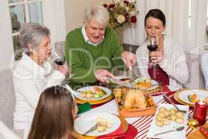 Grandfather carving chicken while women drinking red wine